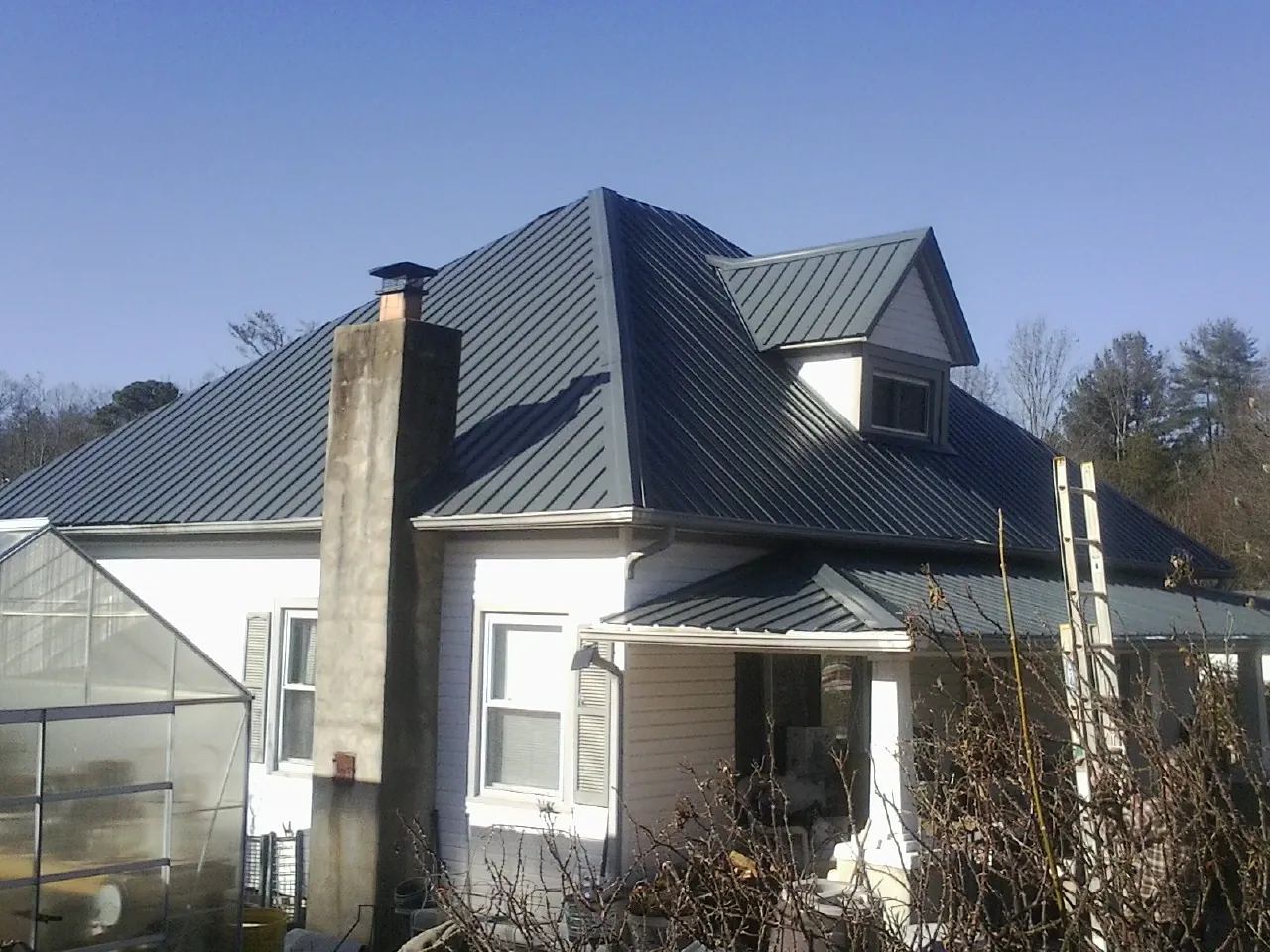 Dark blue standing seam metal roof on a white farmhouse with dormer — Slate & Tile Roof Repair by Roofing Brothers in Manitou Beach