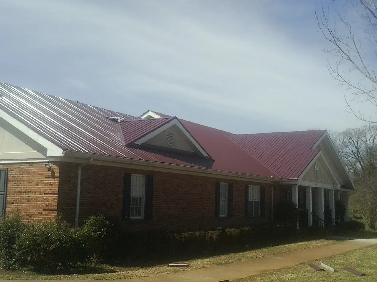 Red metal roof with gabled entries on a long brick building, from a Hail Damage Roof Repair job in Manitou Beach