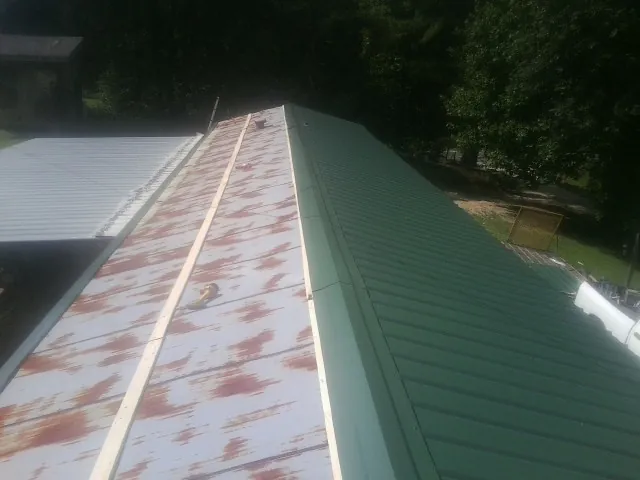 Old rusted panels beside newly installed green metal roofing — Wind Damage Roof Repair by Roofing Brothers in Manitou Beach