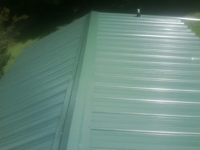 New green metal panels meeting at the ridge of a roof — Flat Roof Repair work by our crew in Manitou Beach