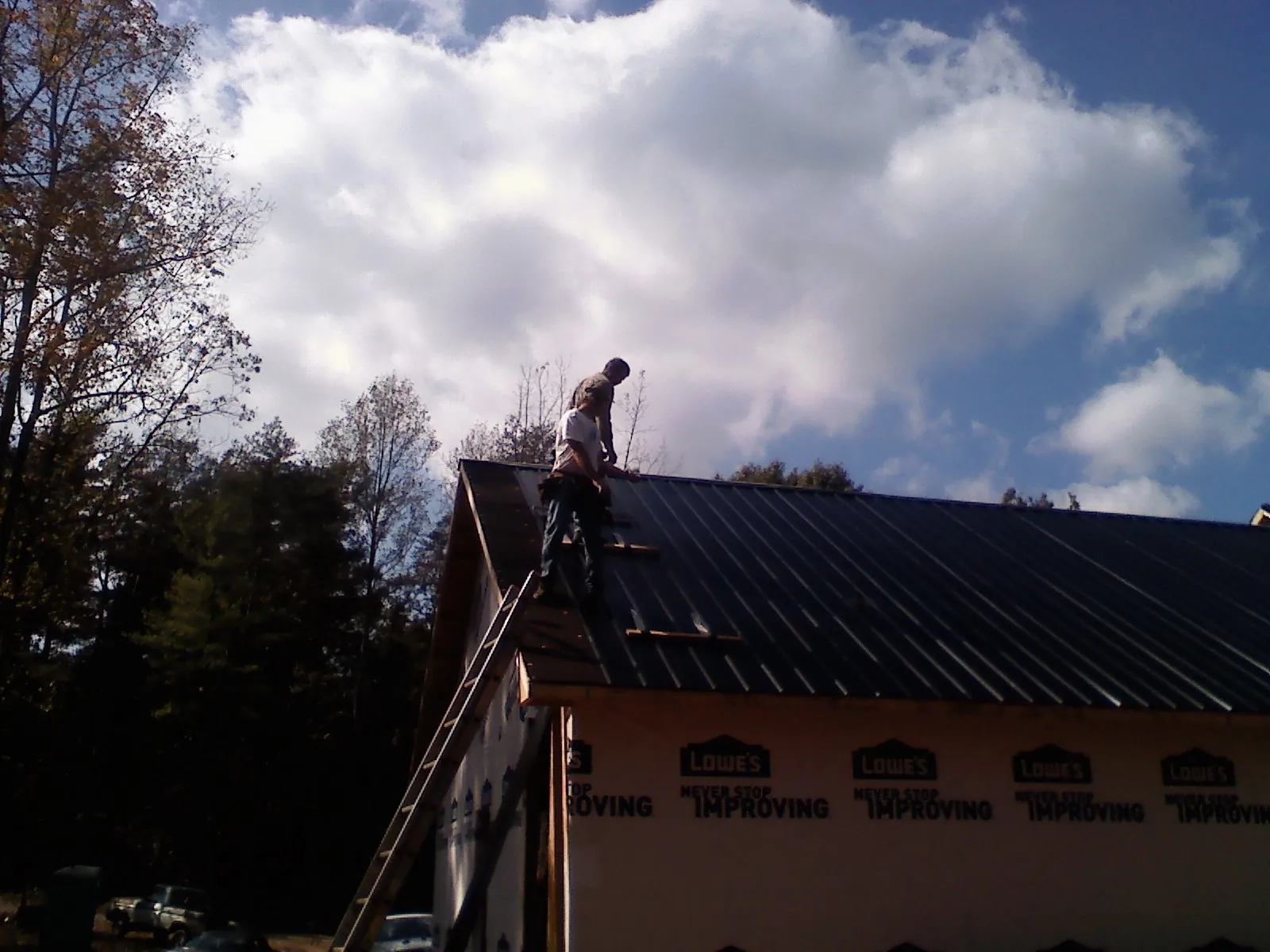 Roofer fastening dark metal panels high against a cloudy sky, from a Roof Inspection job in Manitou Beach