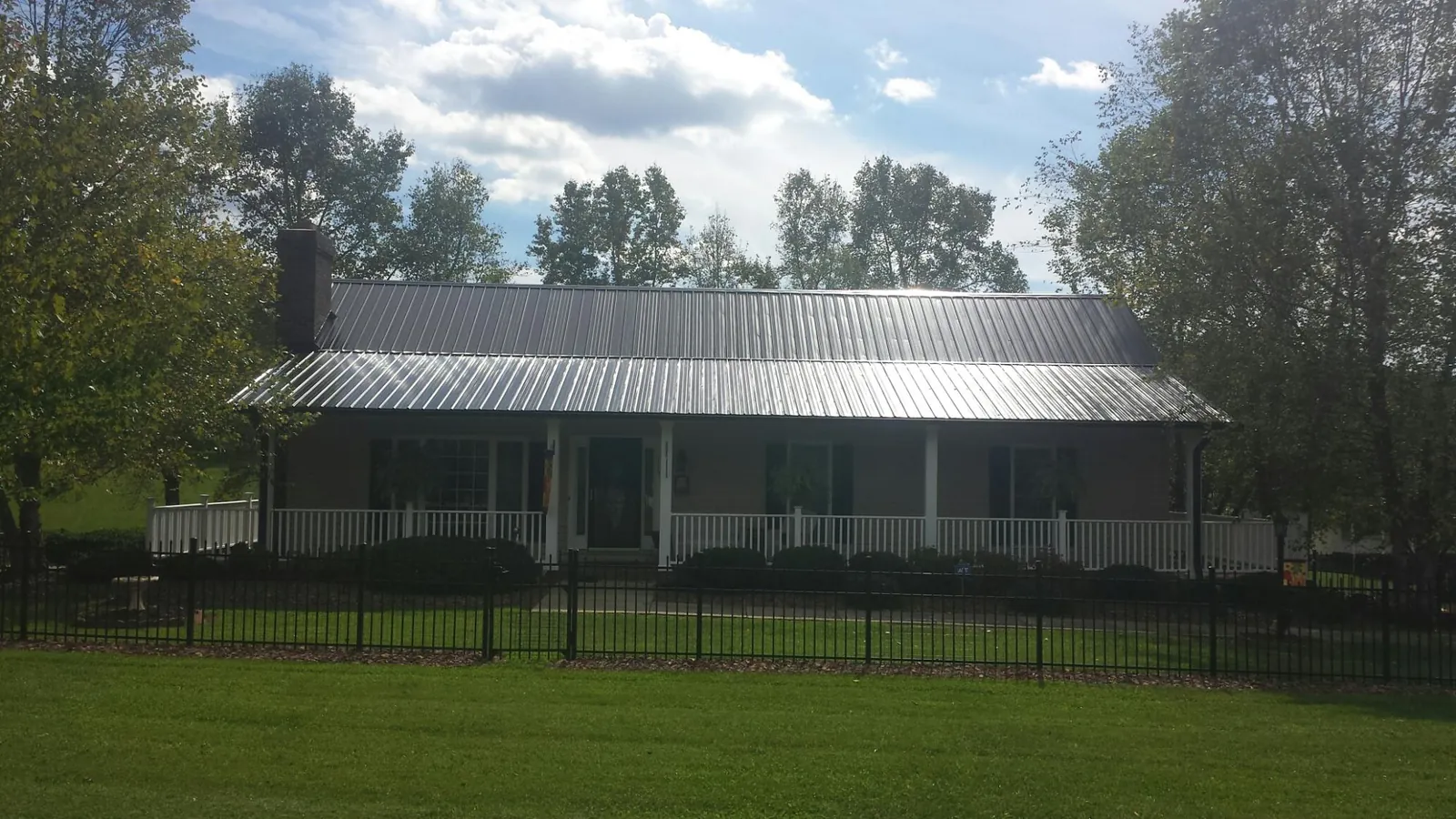 Gray metal roof on a brick ranch with a full width front porch — Gutter Guard Installation work by our crew in Manitou Beach