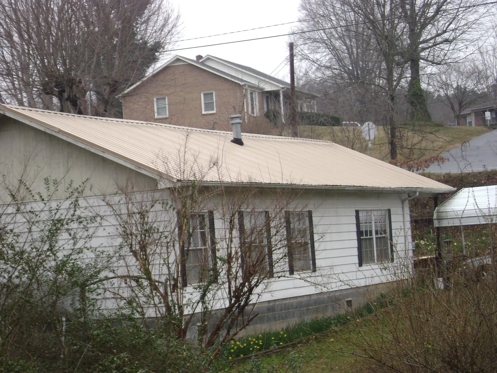 Tan metal roof on a white sided house set into a hillside — Commercial Roofing by Roofing Brothers in Manitou Beach