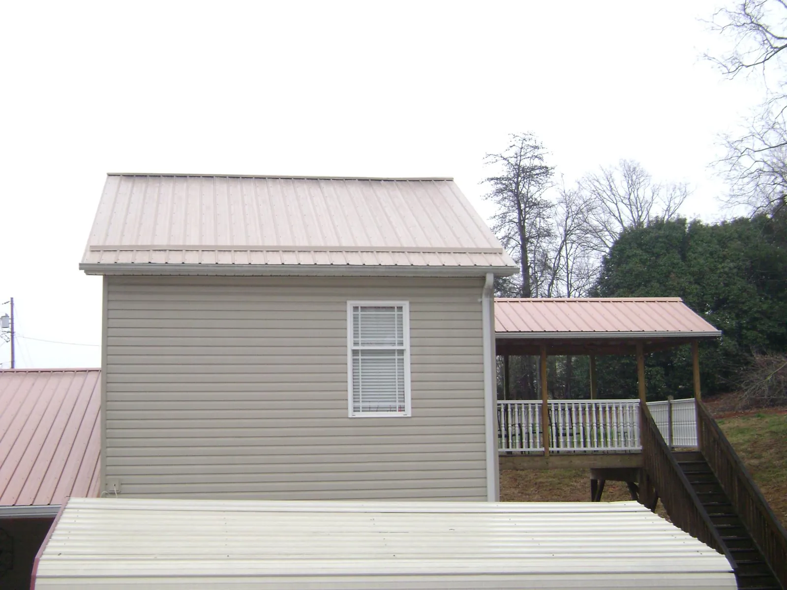 Tan metal roofs on a two story addition and attached porch, from a Roof Replacement job in Manitou Beach